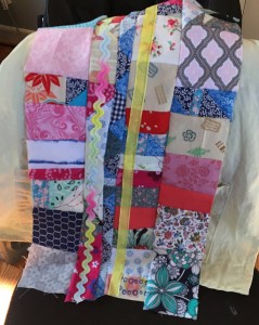 I dyed a pre-made blank canvas apron a very light citron color and I draped my piecing over it to check and see if the colors are ok together. To the front of the pieced section I sewed some translucent yellow trim and a piece of pastel rainbow rick-rack to tie the colors together.